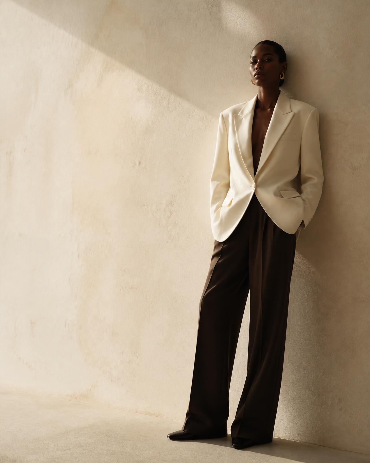 Client styled in a cream tailored blazer and espresso trousers against a warm plaster wall